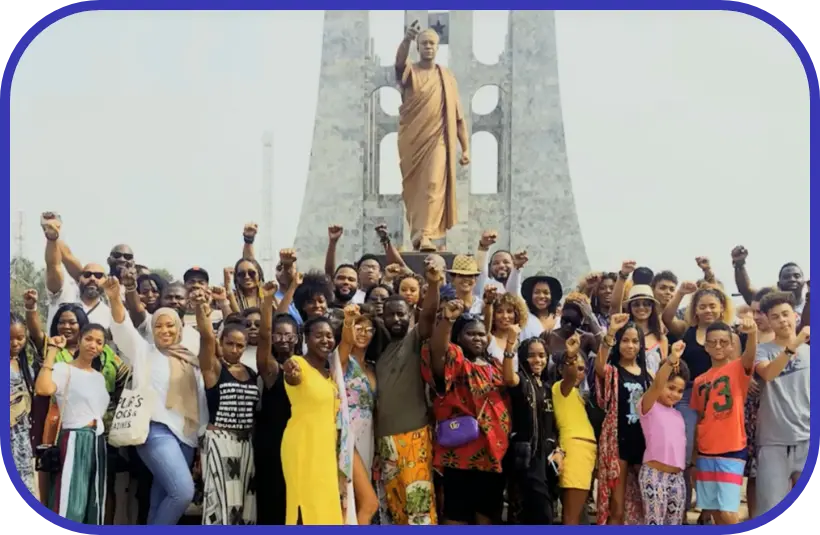 A large group of people with arms raised standing in front of a statue.